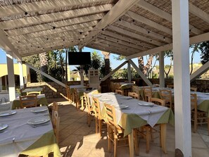 An outdoor dining area with tables and chairs, a TV screen, and a stone wall. - Il Trappeto (Gallipoli)