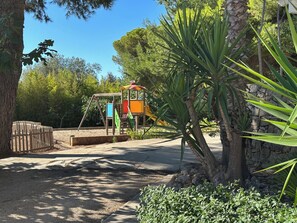A playground with a slide and swings, surrounded by trees and a stone wall. - Il Trappeto (Gallipoli)