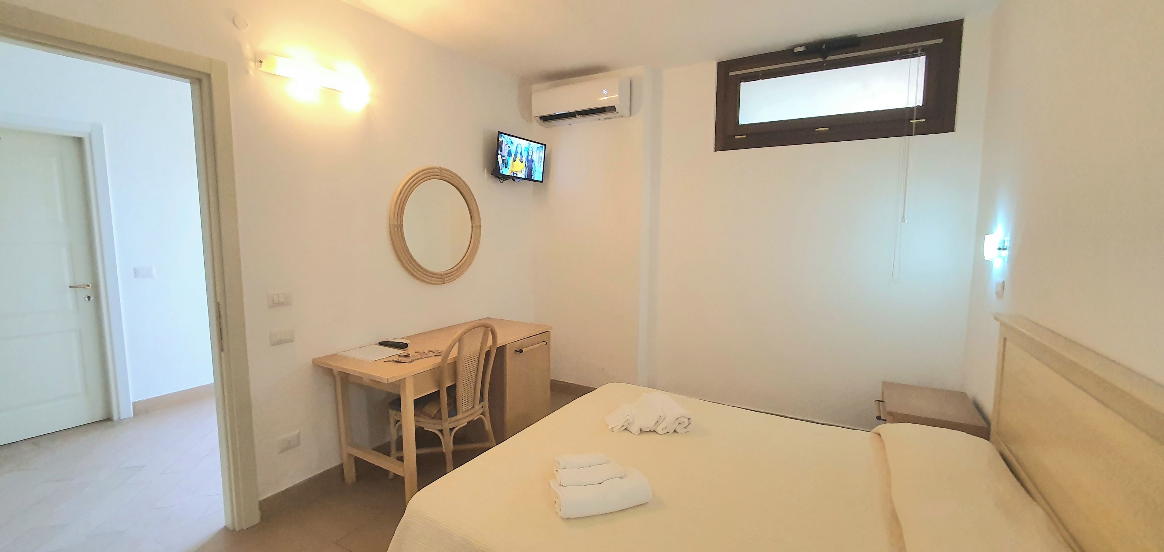 A hotel room with a bed, a desk with a chair, a television, and a window.