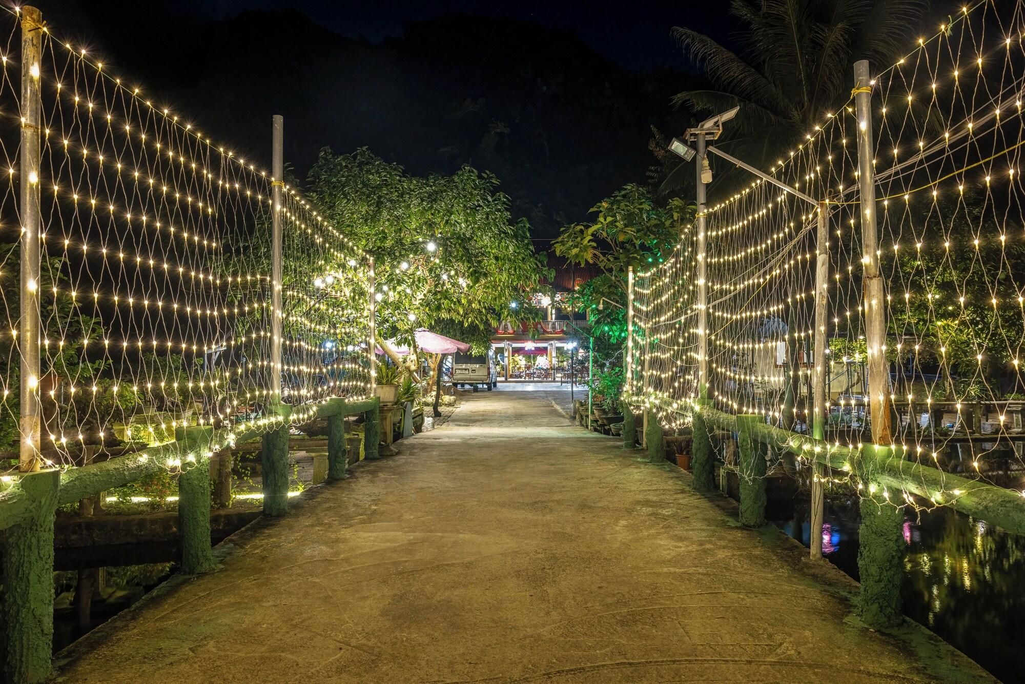 A pathway lined with string lights and trees, leading to a building with a red roof.