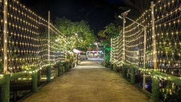A pathway lined with string lights and trees, leading to a building with a red roof.
