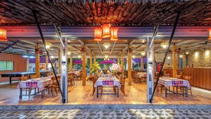Un restaurant intérieur avec des tables et des chaises en bois, une table de billard et des luminaires suspendus.