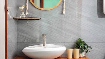 A bathroom with a wooden vanity, a white sink, a round mirror with a rope handle, and a potted plant.