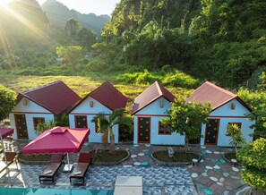 Un complejo turístico con tres villas, cada una de techo rojo y paredes blancas, rodeado de exuberante vegetación y un área de piscina.
