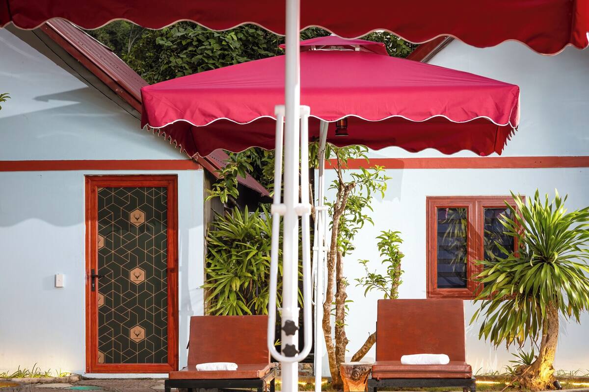 Un espace aménagé au bord de la piscine, avec des chaises longues, une piscine et un parasol rouge.