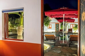 Een terras buiten met een rode parasol, een pooltafel en een terras met stenen tegels.