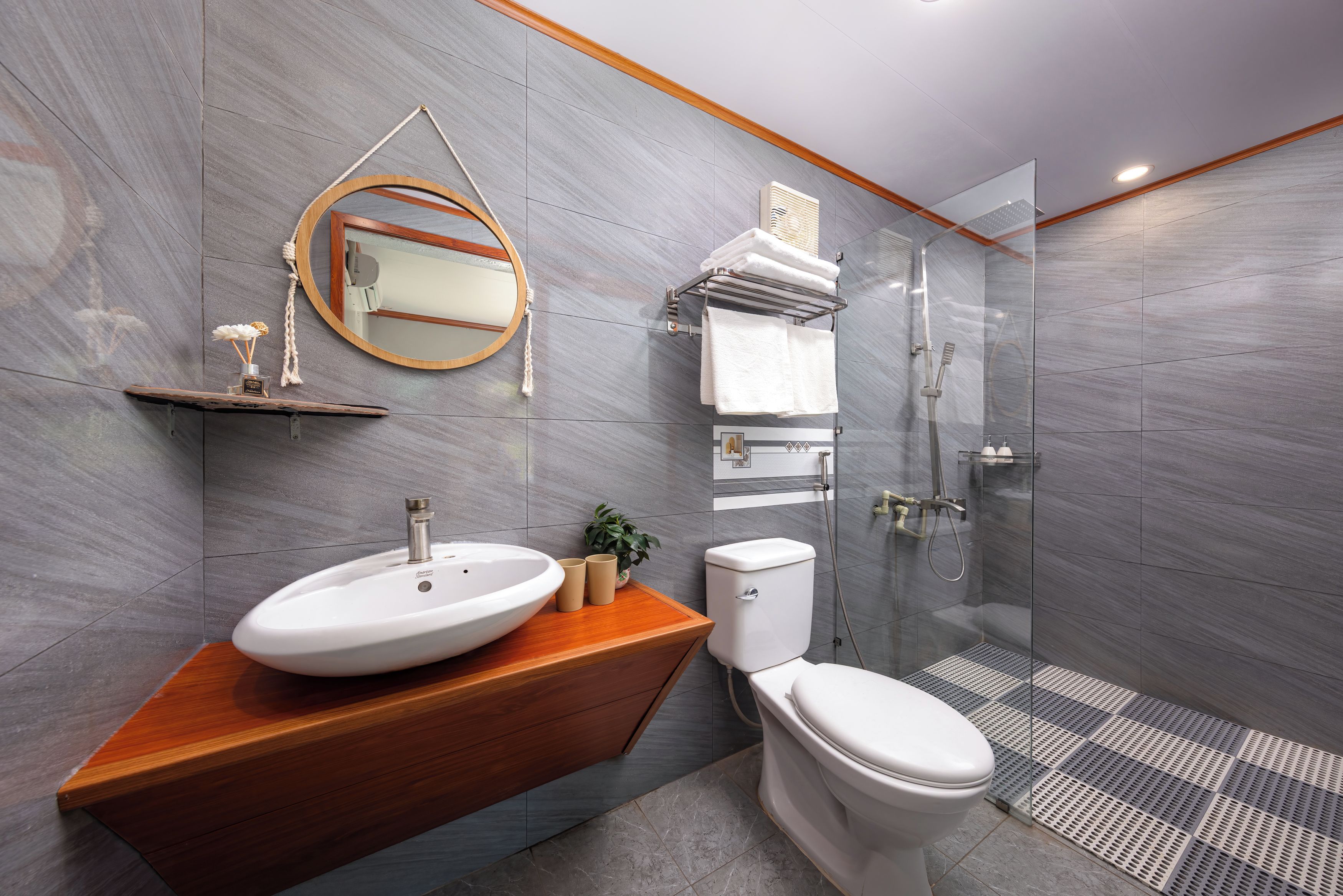 A modern bathroom with a wooden vanity, a round mirror, a toilet, and a glass-enclosed shower.