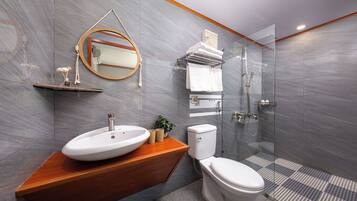 A modern bathroom with a wooden vanity, a round mirror, a toilet, and a glass-enclosed shower.