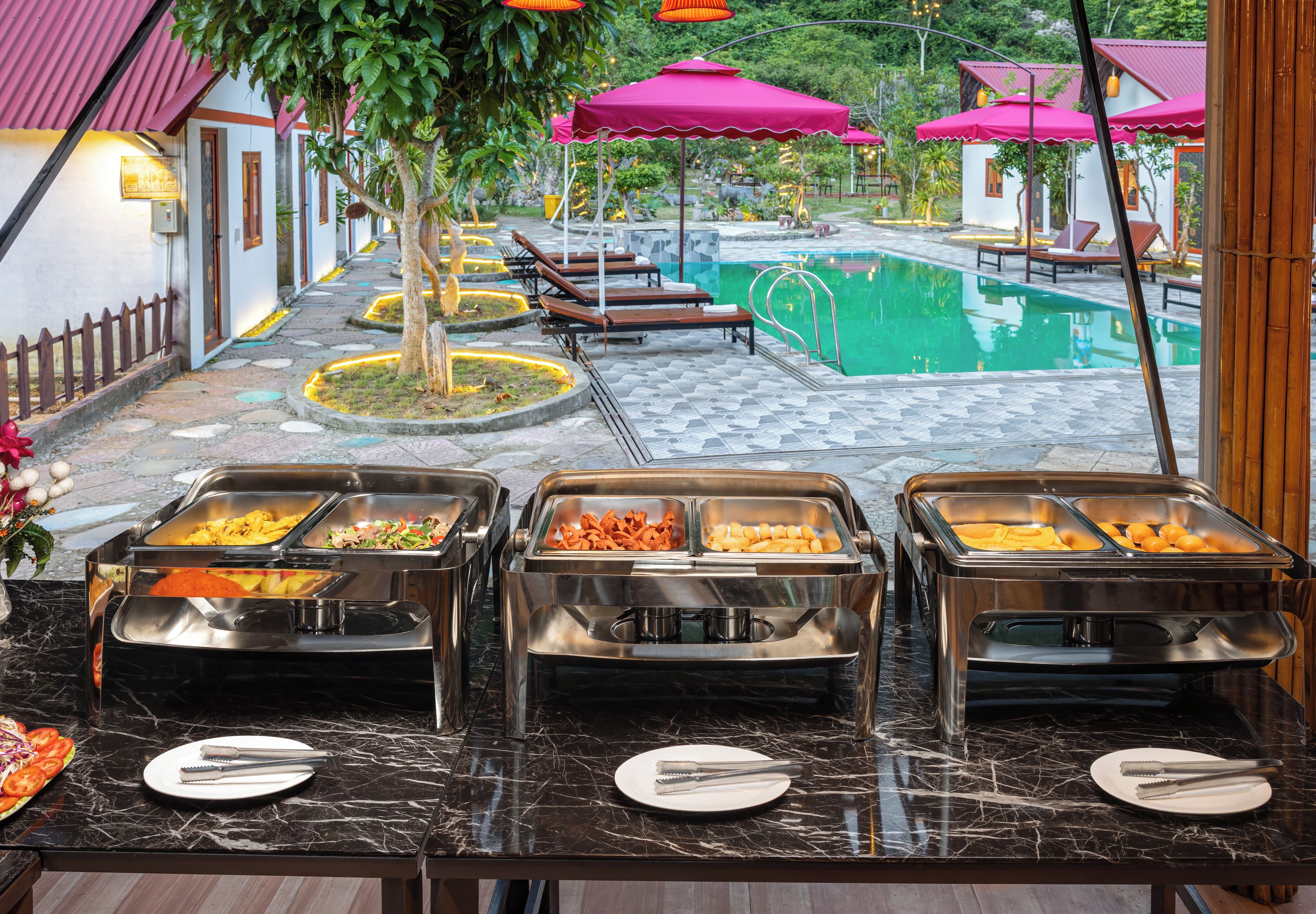 A buffet area with multiple food stations, a pool, and lounge chairs.