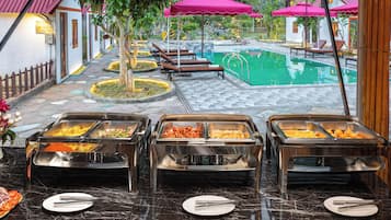 A buffet area with multiple food stations, a pool, and lounge chairs.