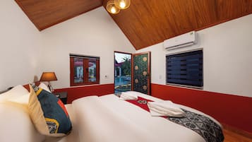 A hotel room with a wooden ceiling, a bed with white bedding, a red wall, and a window with blinds.