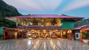 A restaurant with a covered outdoor seating area, a staircase, and a view of the surrounding greenery. - Cat Ba Serena Homestay And Swimming Pool (Cat Hai)