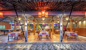 Un restaurante interior con mesas y sillas de madera, una mesa de billar y luces colgantes.