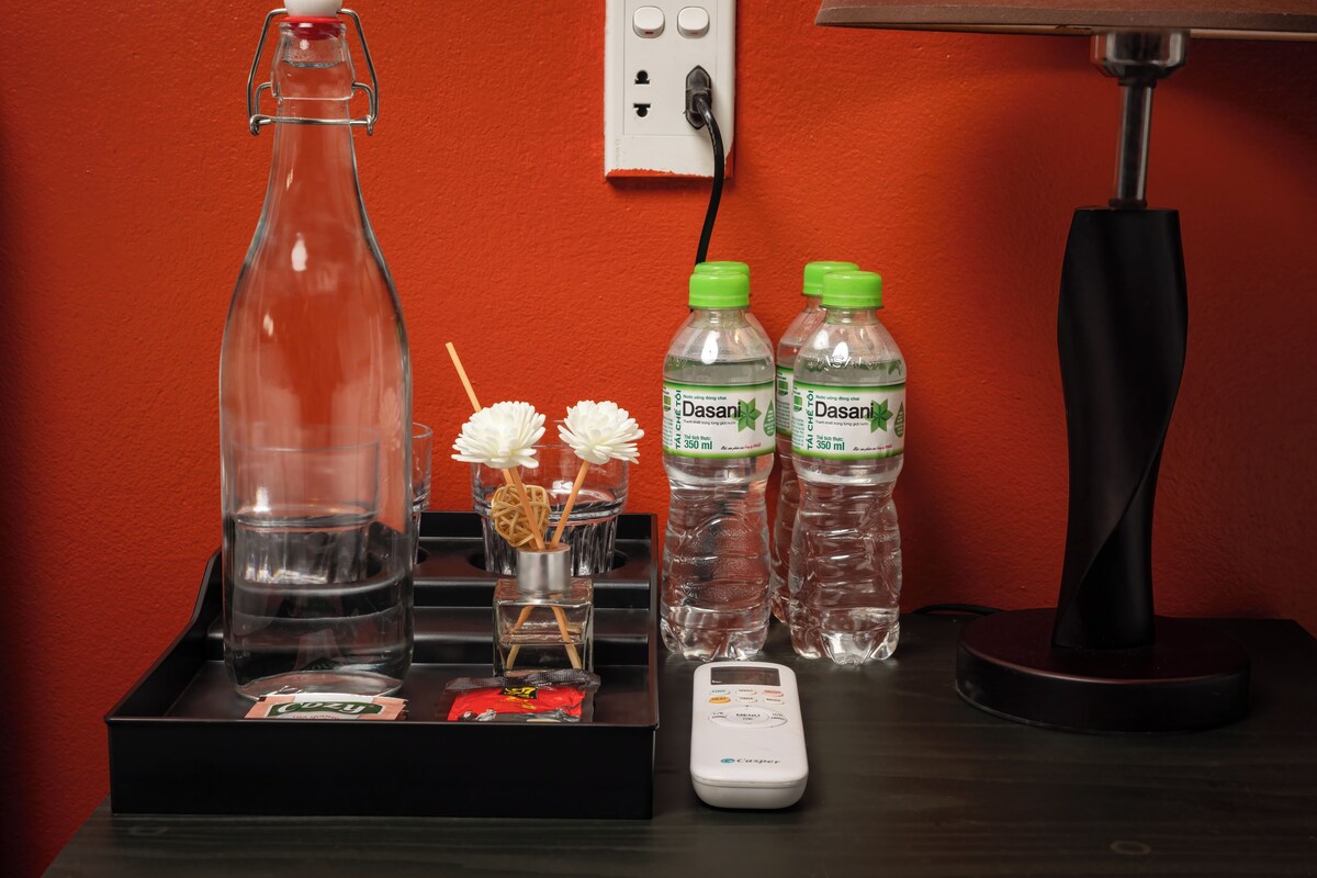 Una habitación de hotel con minibar, una botella de agua Dasani, una botella de Cheetos, un recipiente de vidrio y una balanza digital.