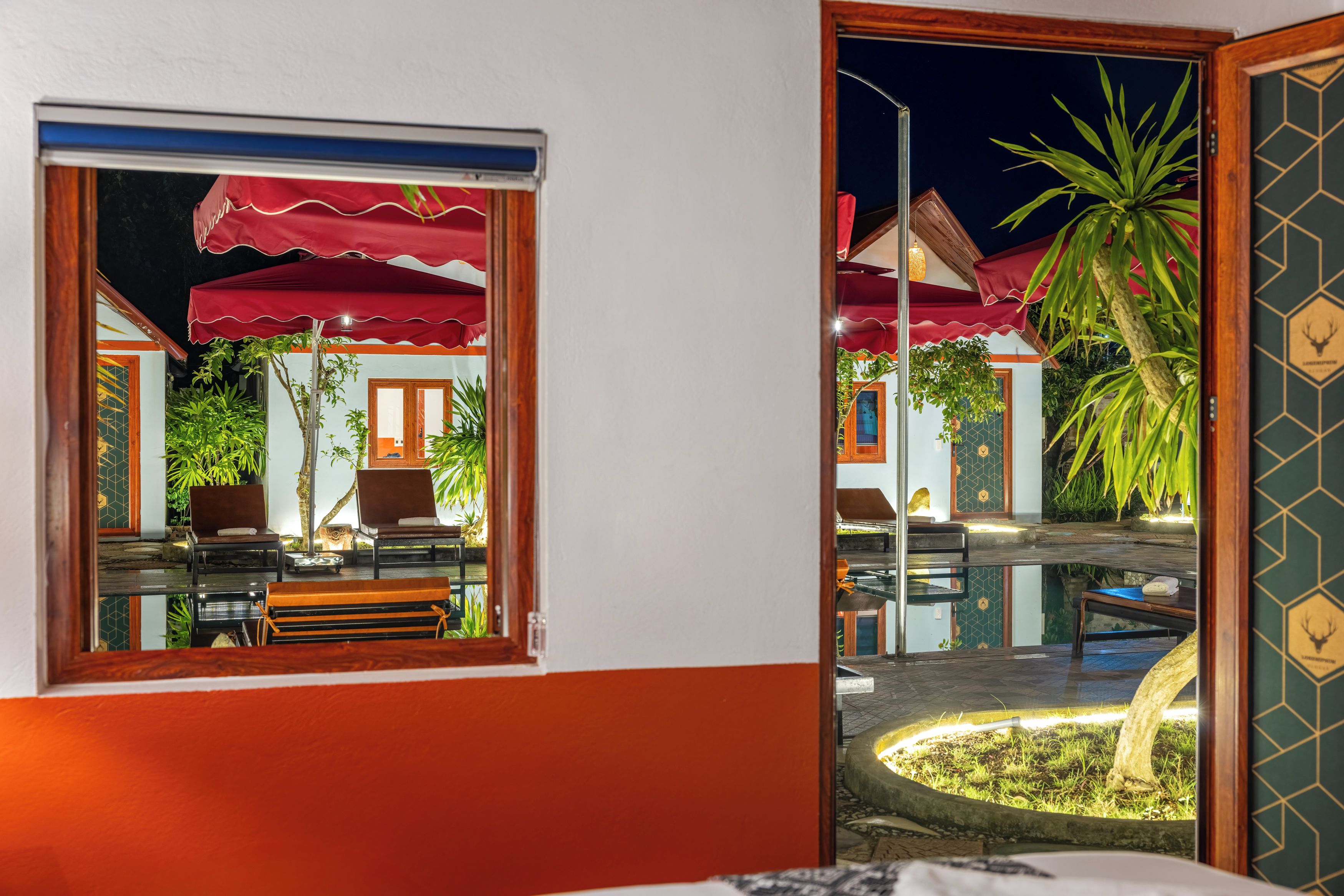 Habitación con ventana que da a un patio con piscina, sillas y sombrillas.