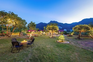 Un espace extérieur bien aménagé, doté de coins salon et d’arbres, et entouré de montagnes.