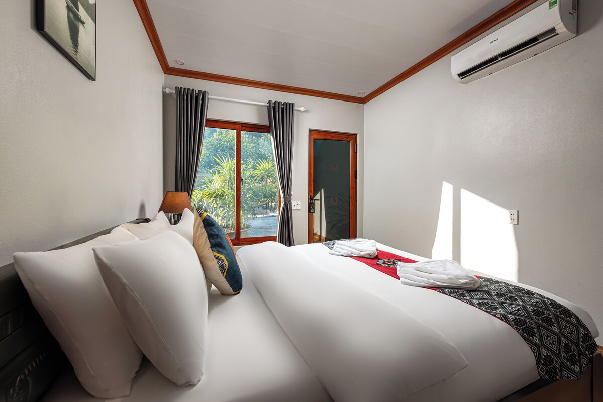 Une chambre d’hôtel avec un lit, des oreillers, une fenêtre avec des rideaux, un appareil de climatisation et une porte.