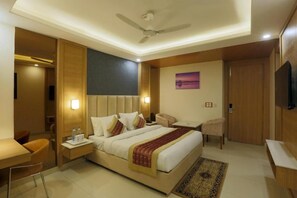 A hotel room with a bed, bedside tables, a desk, a chair, a television, and a ceiling fan. - Hotel Sakura By Maps, Huda City Center (Gurugram)