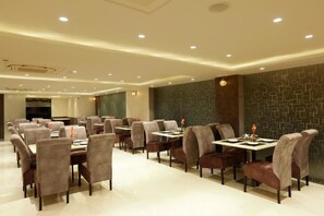 A modern dining area with tables and chairs, recessed ceiling lighting, and a patterned wall. - Hotel Sakura By Maps, Huda City Center (Gurugram)