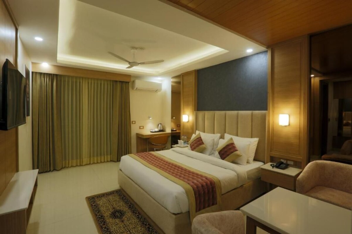 A hotel room with a large bed, a desk, a chair, a television, and a ceiling fan.