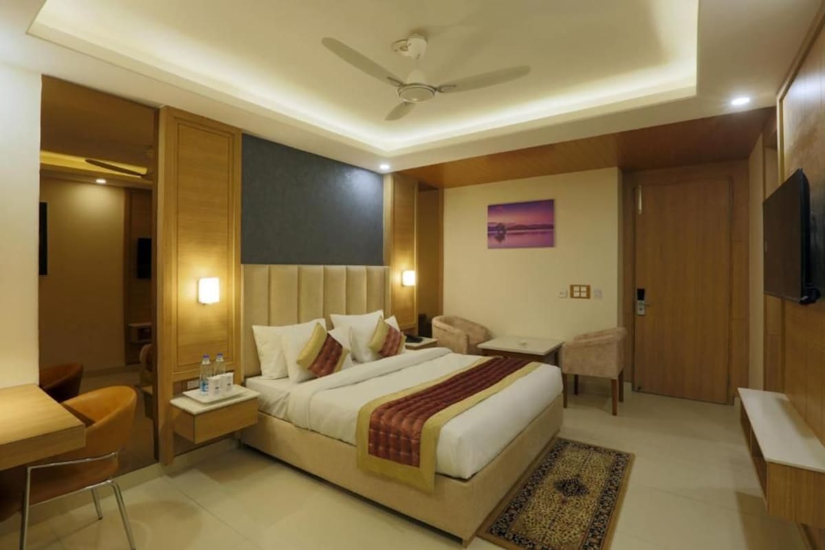A hotel room with a bed, bedside tables, a desk, a chair, a television, and a ceiling fan.
