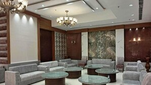 A modern lounge area with sofas and round tables, a chandelier, and a marble wall. - Hotel Sakura By Maps, Huda City Center (Gurugram)