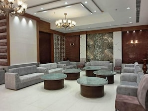 A modern lounge area with sofas and round tables, a chandelier, and a marble wall. - Hotel Sakura By Maps, Huda City Center (Gurugram)