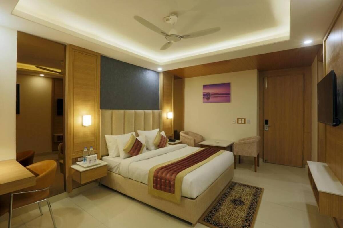 A hotel room with a bed, bedside tables, a desk, a chair, a television, and a ceiling fan.