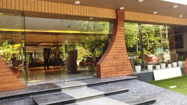 A modern building entrance with glass doors, a wooden ramp, and a well-maintained lawn. - Hotel Sakura By Maps, Huda City Center (Gurugram)