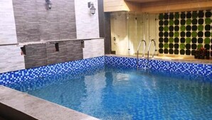 A swimming pool with blue mosaic tiles and a glass enclosure. - Hotel Sakura By Maps, Huda City Center (Gurugram)