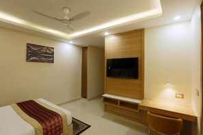 Une chambre à coucher comprenant un lit, un bureau, une chaise, un téléviseur et un ventilateur de plafond.