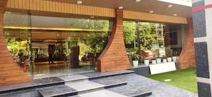 A modern building entrance with glass doors, a wooden ramp, and a well-maintained lawn. - Hotel Sakura By Maps, Huda City Center (Gurugram)