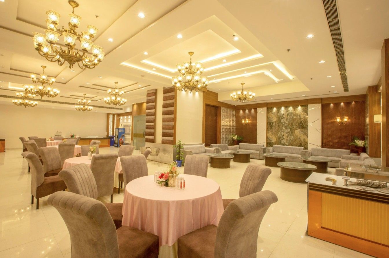 A spacious hotel lobby with multiple seating areas, including round tables and sofas, and a reception desk.