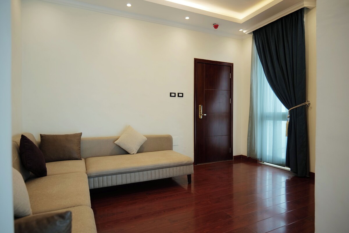 A living room with a beige sofa, dark curtains, and a wooden floor.