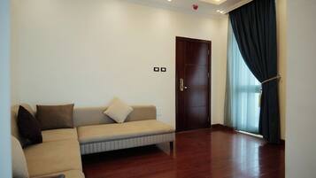 A living room with a beige sofa, dark curtains, and a wooden floor.