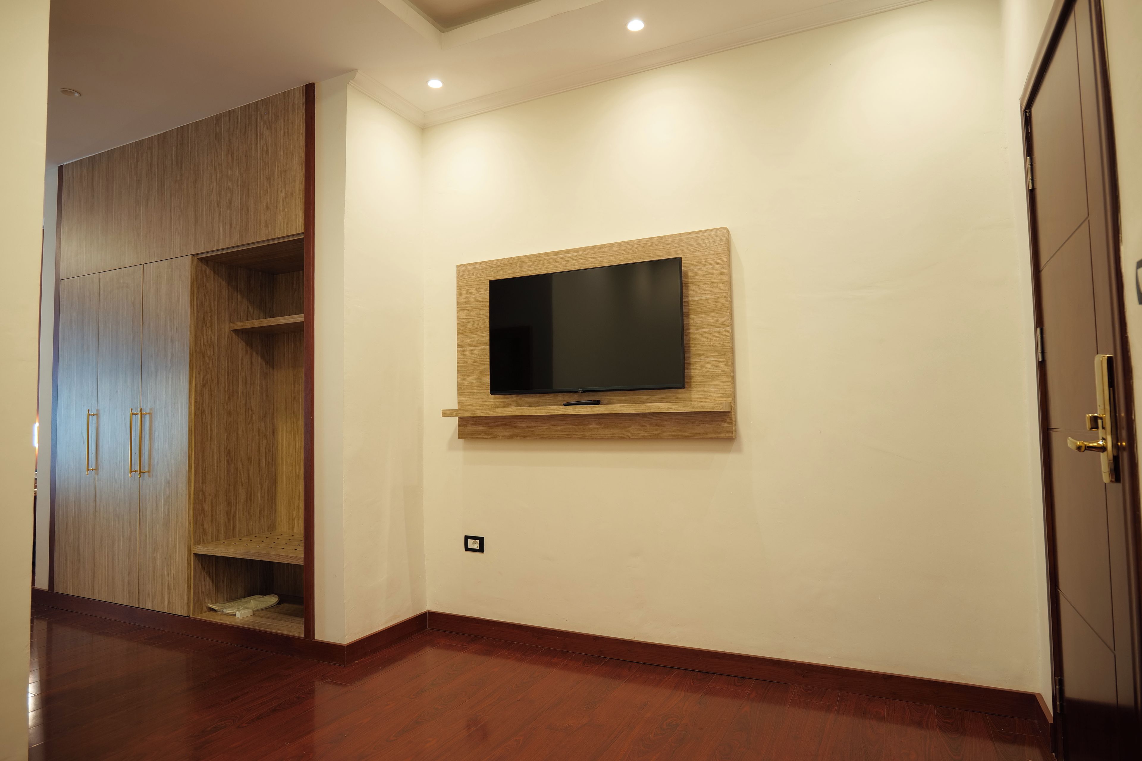 A room with a wooden wardrobe, a mounted TV, and a door.