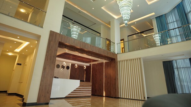 A spacious lobby with a grand chandelier, a wooden reception desk, and a staircase leading to an upper level. - Crescent International Hotel Bole (Addis Ababa)