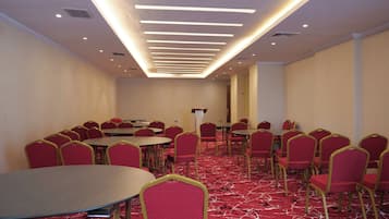 A conference room with round tables and red chairs, a red carpeted floor, and a modern ceiling with recessed lighting.