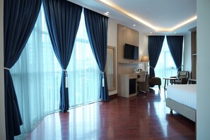 A hotel room with a large bed, a desk with a chair, a TV mounted on the wall, and large windows with curtains. - Crescent International Hotel Bole (Addis Ababa)