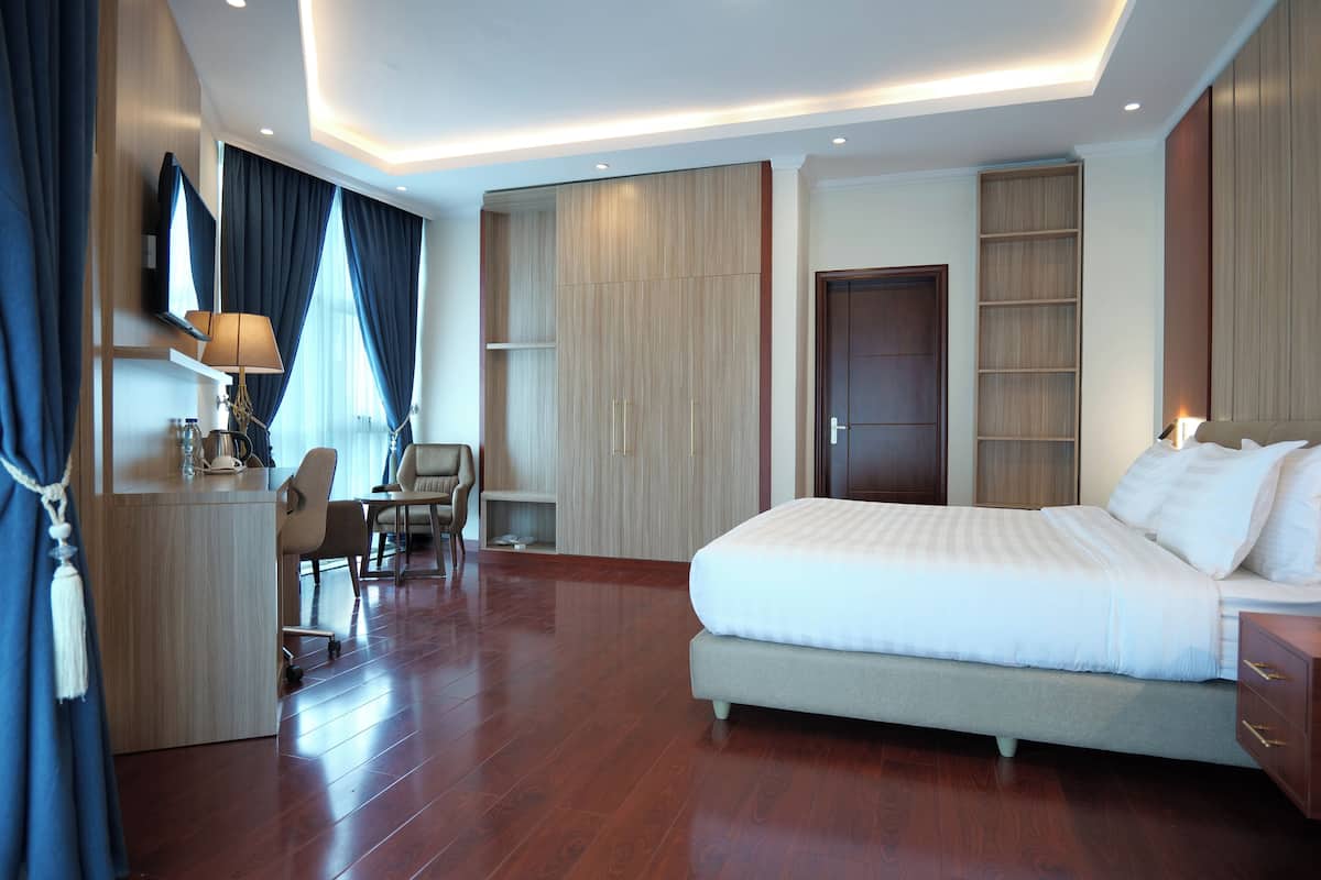 A modern hotel room with a large bed, a desk with a chair, a wardrobe, and a TV mounted on the wall.