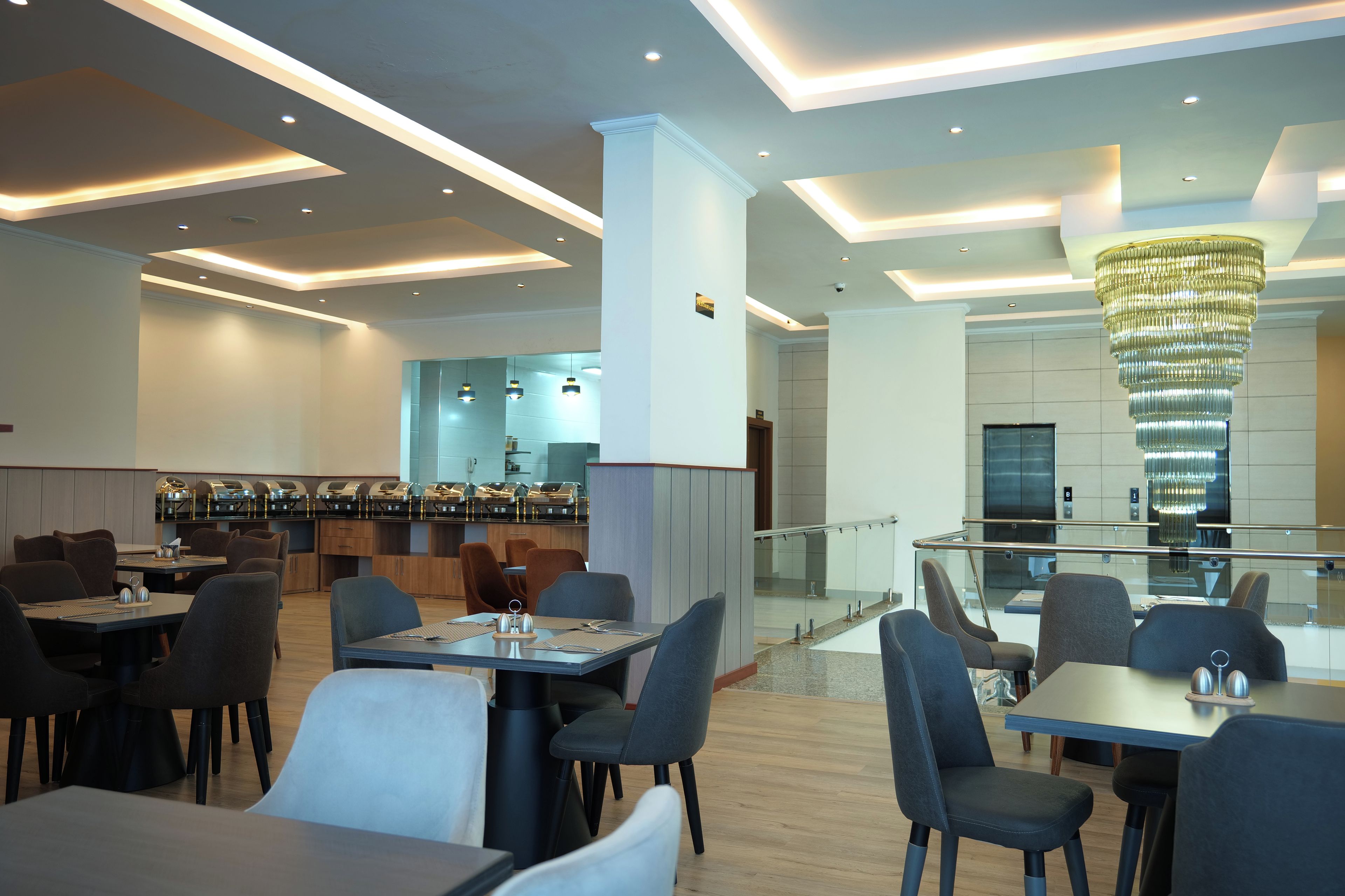 Un espace repas moderne avec des tables et des chaises, un coin bar avec un comptoir et un grand lustre.