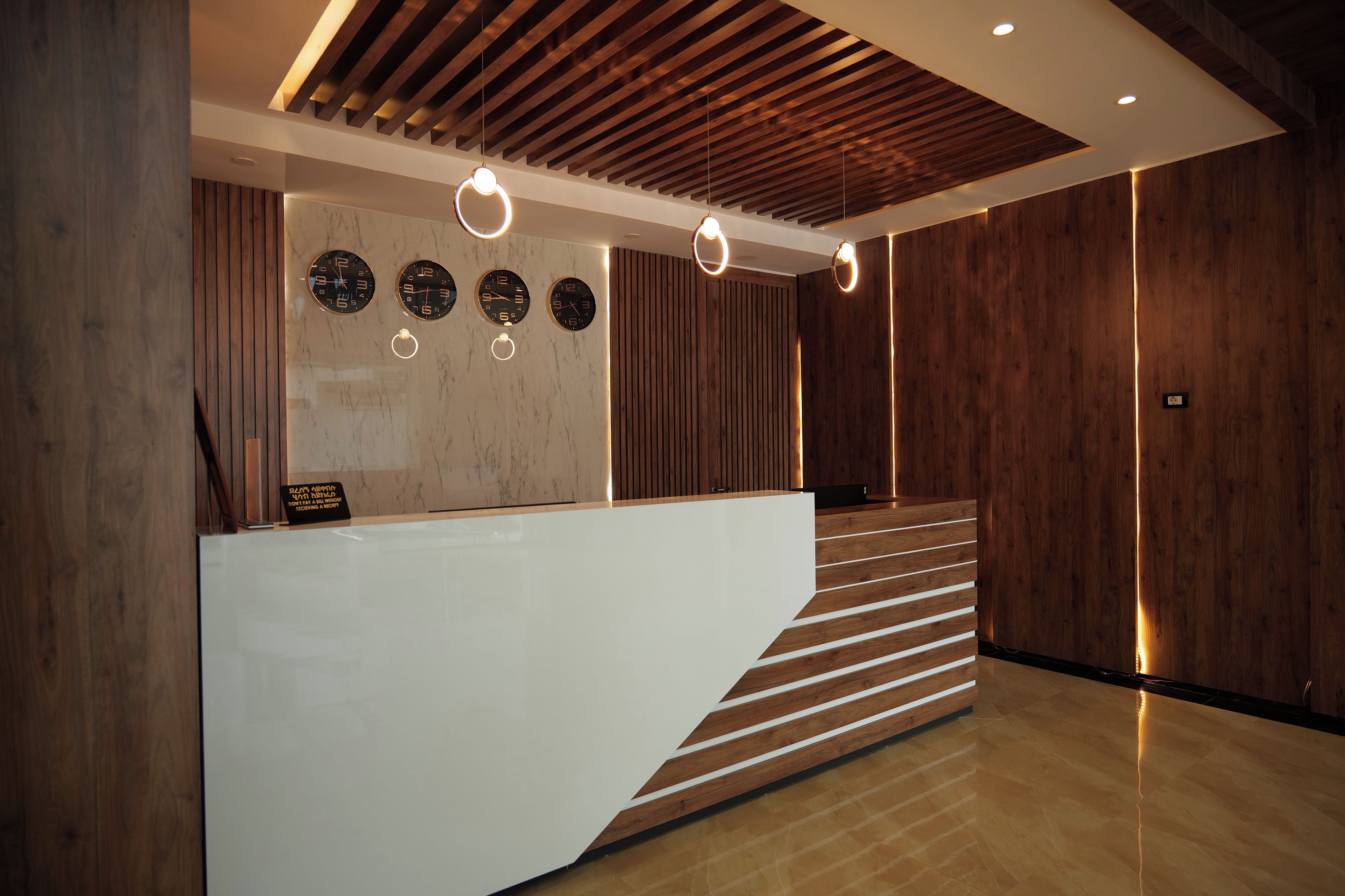 A reception area with a white reception desk, wooden slats, and circular wall clocks.