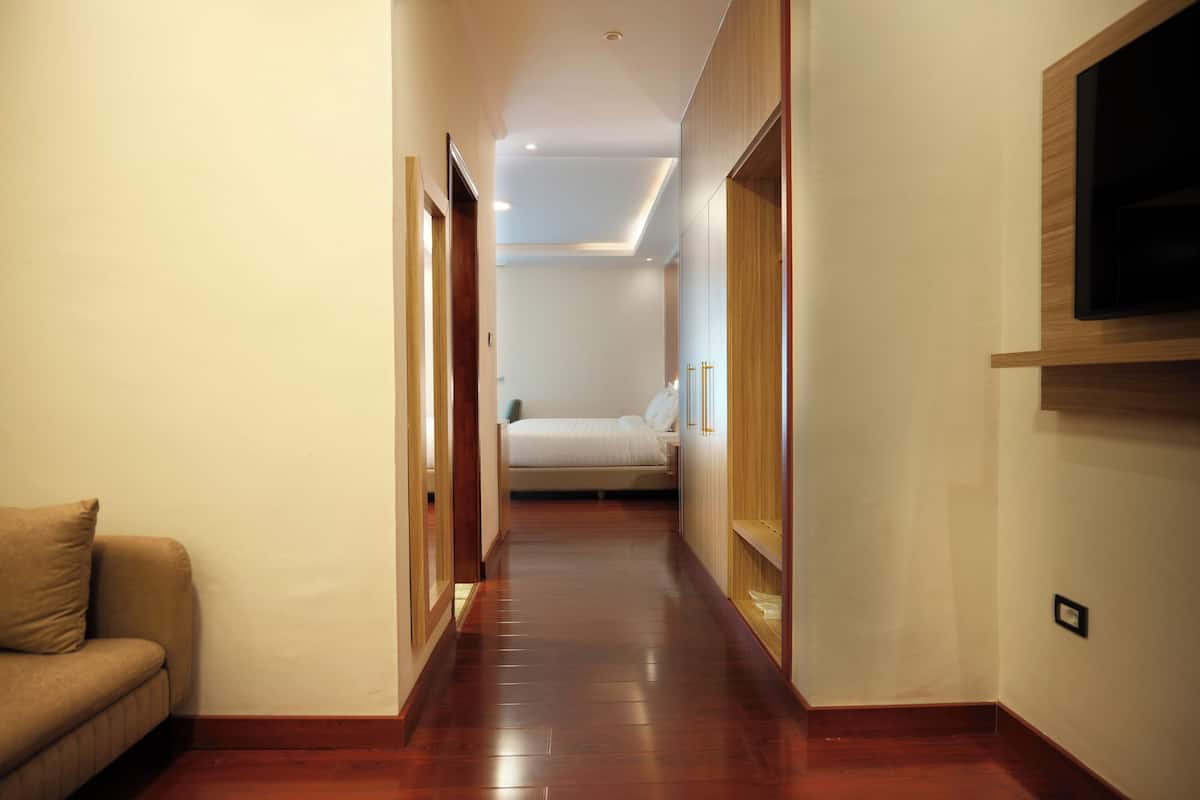 A hallway with wooden flooring, a bed in the background, and a TV mounted on the wall.