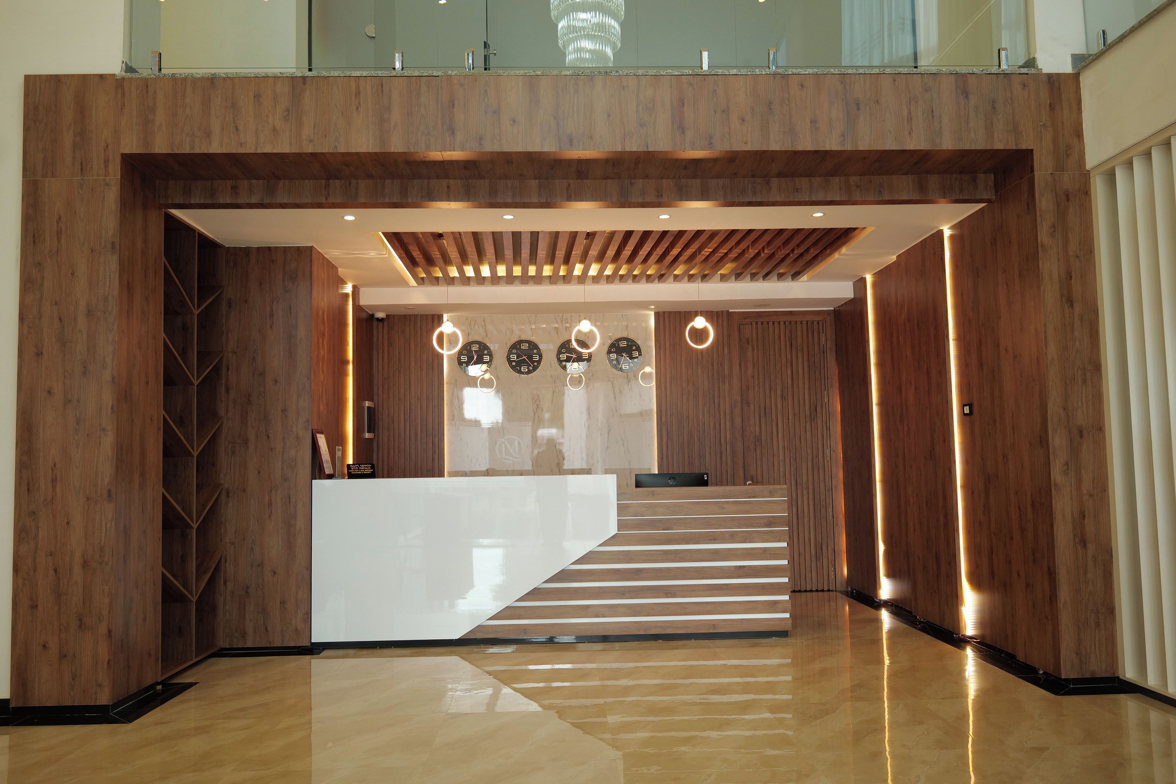 A modern reception area with a wooden reception desk, a staircase, and a chandelier.