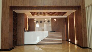 A modern reception area with a wooden reception desk, a staircase, and a chandelier.