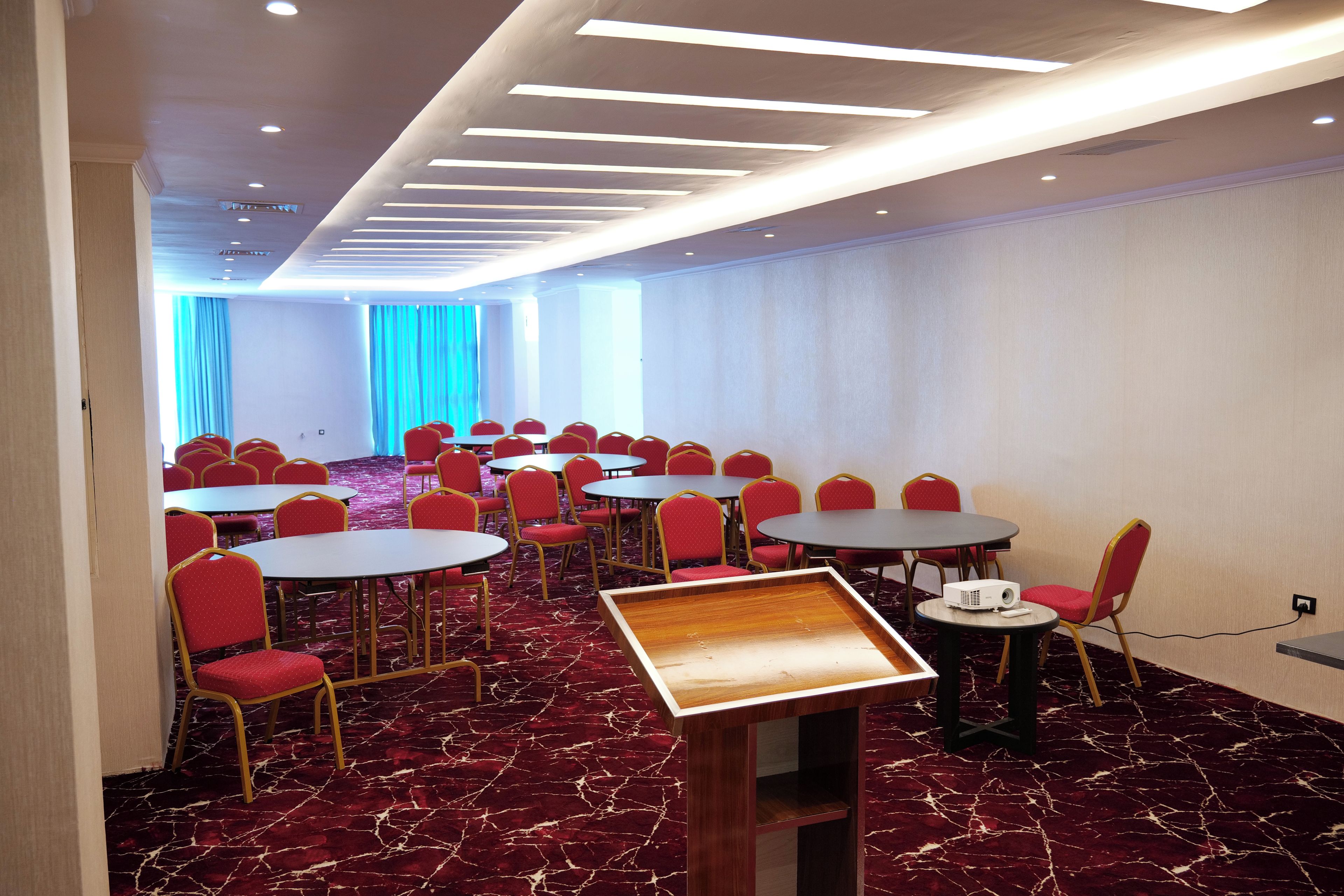 A conference room with multiple tables and chairs, a wooden podium, and a carpeted floor.