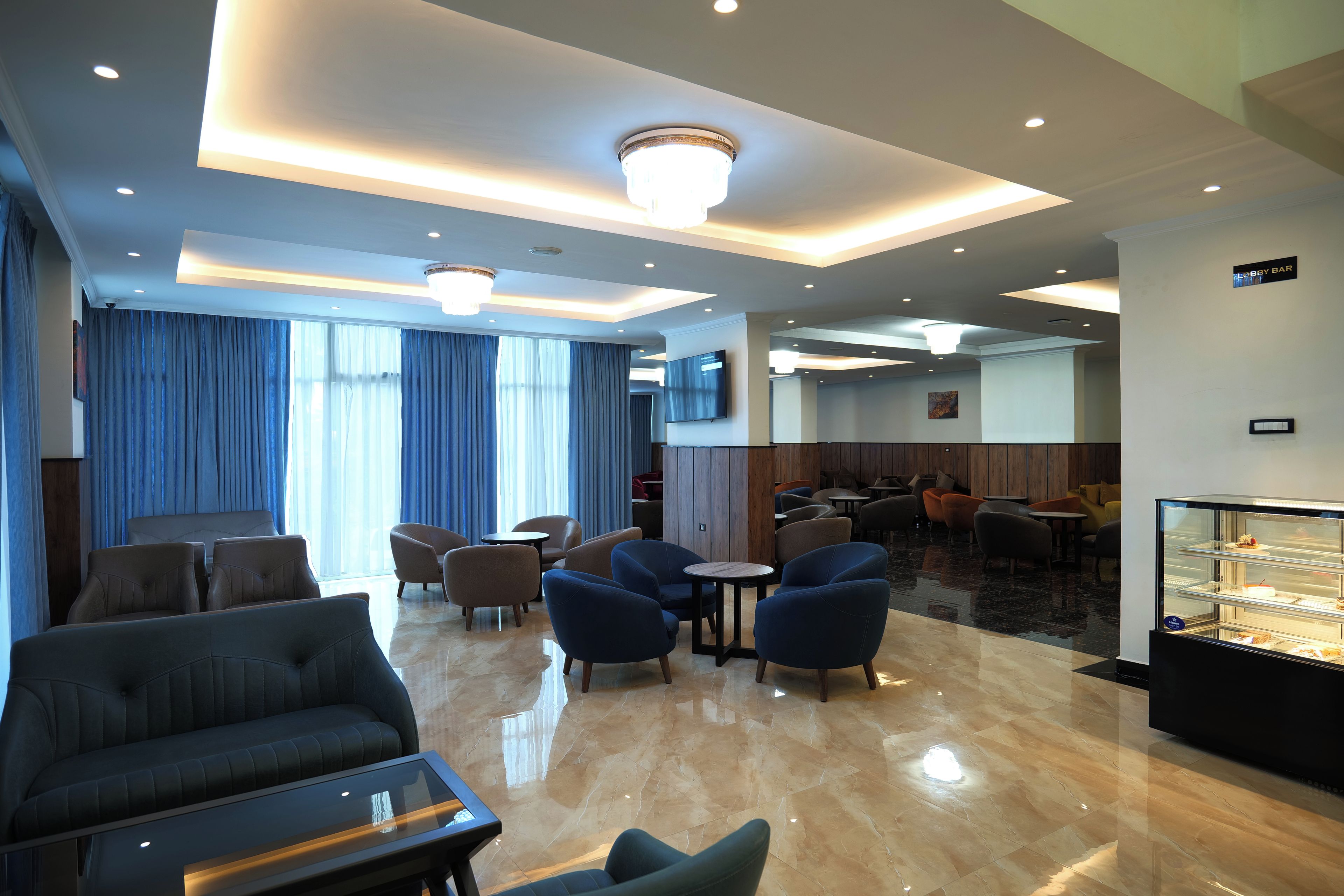 A modern hotel lobby with seating areas, a bar, and a display case.
