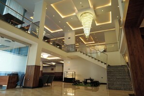A multi-level hotel lobby with a grand chandelier, a staircase, and a reception desk. - Crescent International Hotel Bole (Addis Ababa)