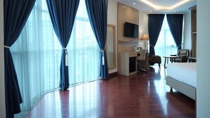 A hotel room with a large bed, a desk with a chair, a TV mounted on the wall, and large windows with curtains. - Crescent International Hotel Bole (Addis Ababa)