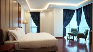 A hotel room with a large bed, a desk, two chairs, and a window with curtains.